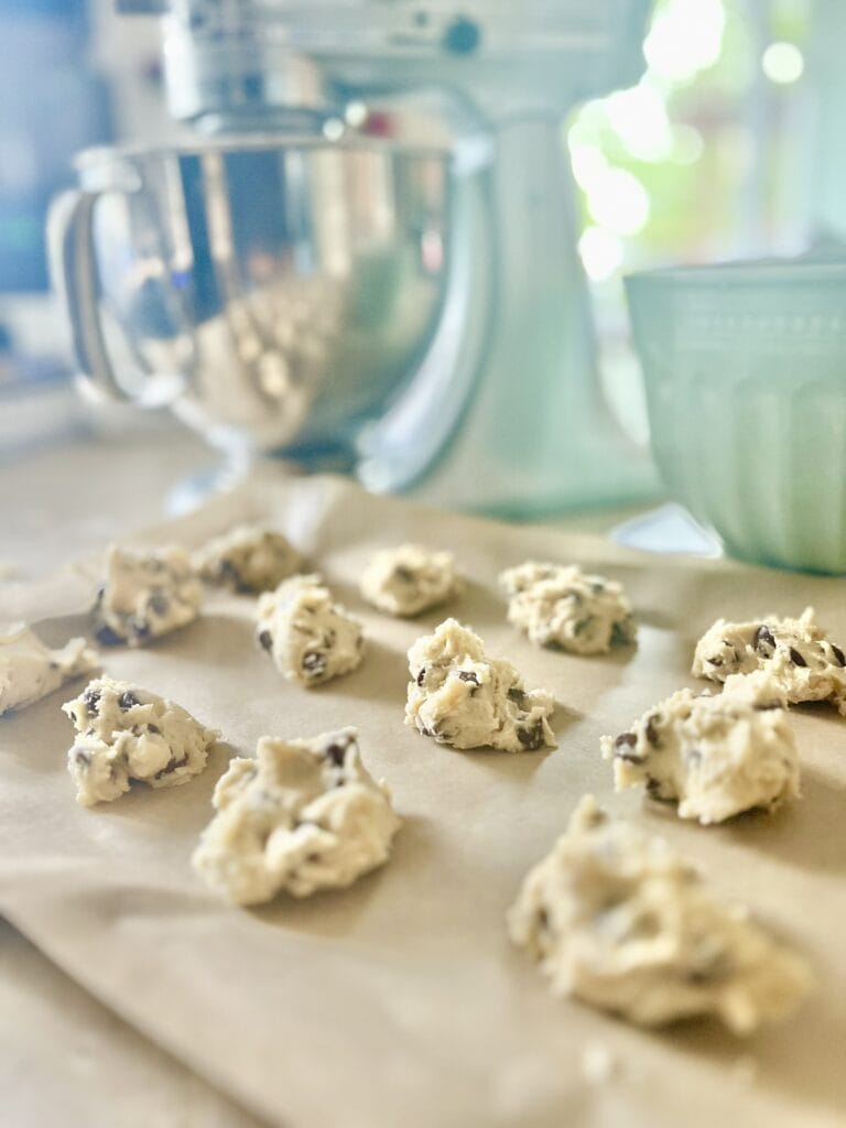 A close-up of chocolate chip cookie dough with visible chocolate chunks, resting on parchment paper, ready to be baked.