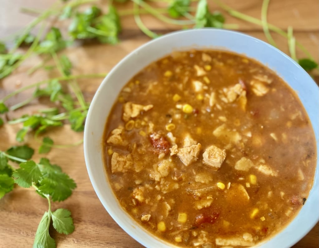 A steaming bowl of chicken tortilla soup garnished with avocado, sour cream, cheese, homemade tortilla strips, and cilantro, showcasing vibrant colors and textures, perfect for a cozy meal