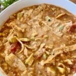 A steaming bowl of chicken tortilla soup garnished with avocado, sour cream, cheese, homemade tortilla strips, and cilantro, showcasing vibrant colors and textures, perfect for a cozy meal