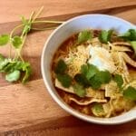 A steaming bowl of chicken tortilla soup garnished with avocado, sour cream, cheese, homemade tortilla strips, and cilantro, showcasing vibrant colors and textures, perfect for a cozy meal