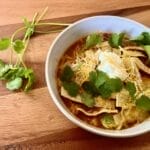 A steaming bowl of chicken tortilla soup garnished with avocado, sour cream, cheese, homemade tortilla strips, and cilantro, showcasing vibrant colors and textures, perfect for a cozy meal