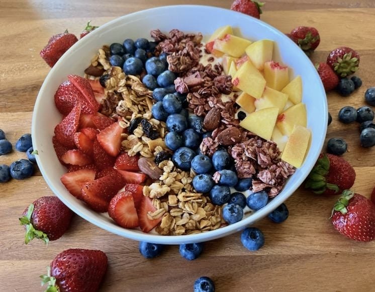 A delicious and visually appealing granola parfait layered with creamy Greek yogurt, fresh strawberries, blueberries, and diced peaches, topped with crunchy granola