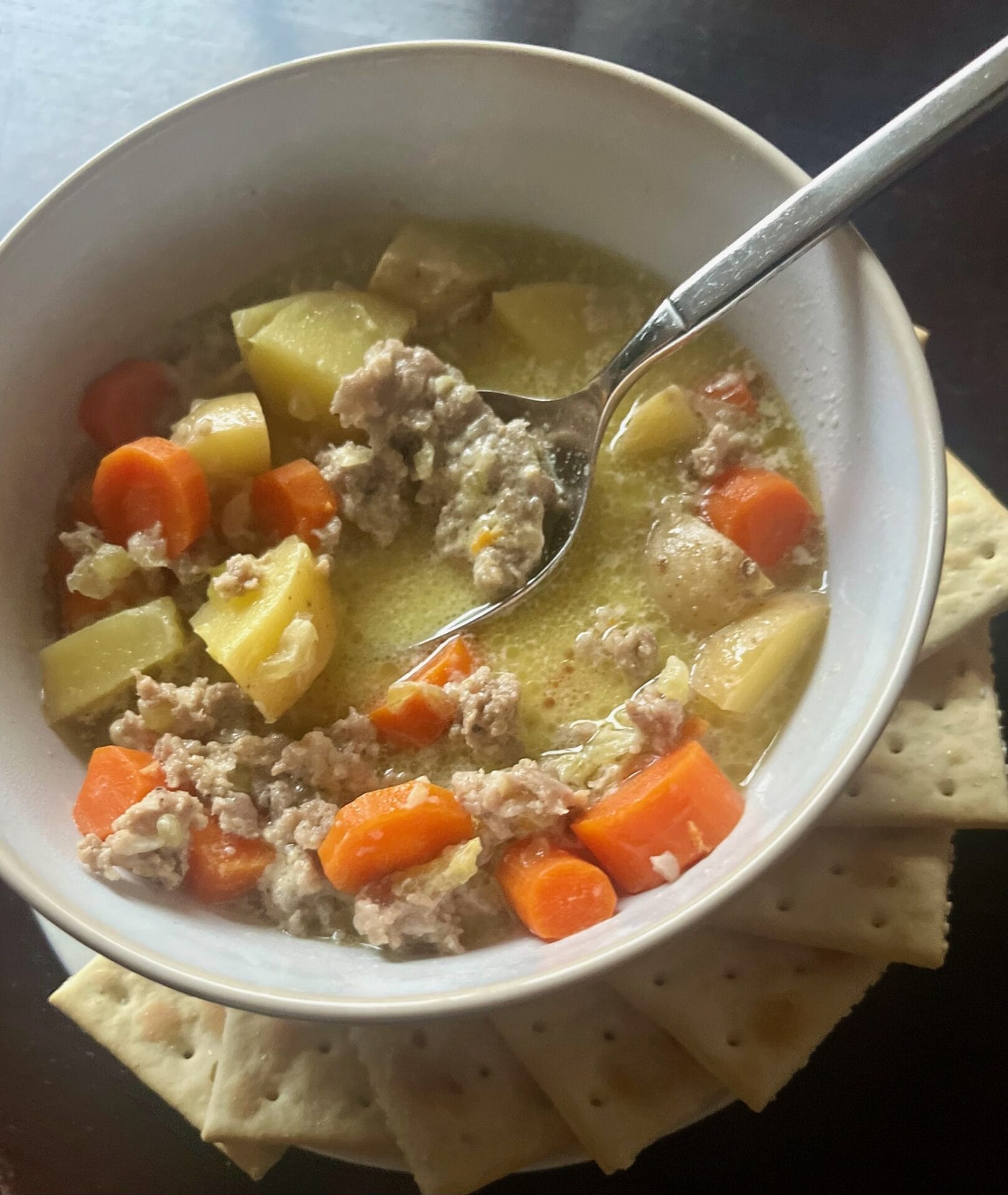 A steaming bowl of Savory Sausage Soup with Potatoes and Carrots, garnished with fresh parsley. The rich broth is filled with slices of sausage, diced potatoes, and tender carrots, showcasing a comforting, hearty meal perfect for cold weather