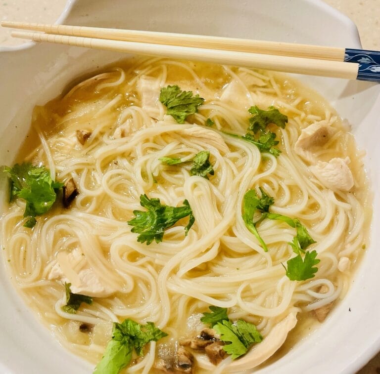 A comforting bowl of Pho-Inspired Chicken Soup featuring tender chicken, mushrooms, onions, and Pho noodles, served steaming hot and ready to enjoy.