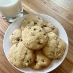 A plate of warm, freshly baked sourdough chocolate chip cookies, topped with a sprinkle of sea salt, accompanied by a glass of cold milk.