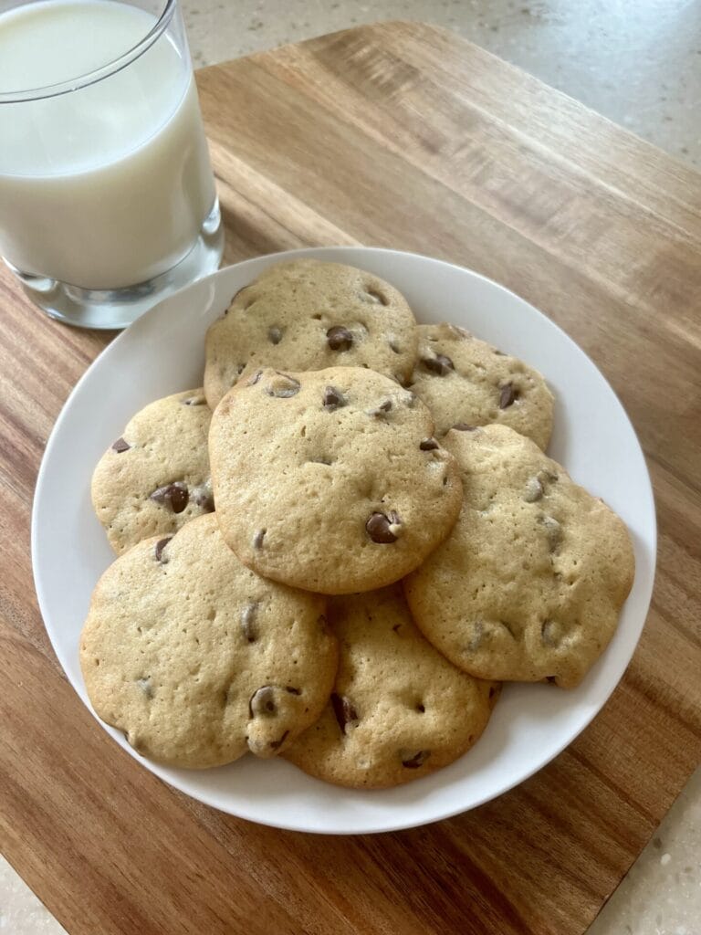 A plate of warm, freshly baked sourdough chocolate chip cookies, topped with a sprinkle of sea salt, accompanied by a glass of cold milk.