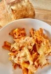 A close-up of a freshly baked ziti casserole in a glass dish, with golden, bubbly cheese on top, garnished with fresh basil leaves. The layers of pasta, sauce, and melted cheese are visible, creating a mouthwatering presentation.