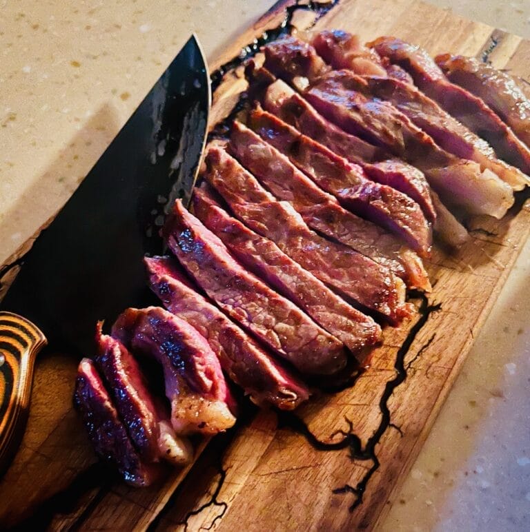 Perfectly cooked Ribeye steak with a crispy crust, seared in a cast iron skillet and finished in the oven, served on a plate with garnish